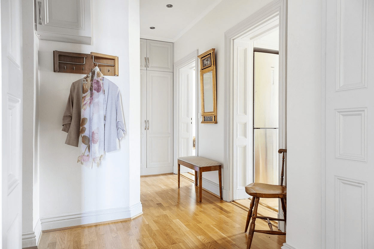 this is a hallway in a Scandinavin apartment with clothes handing and wooden chairs and floors