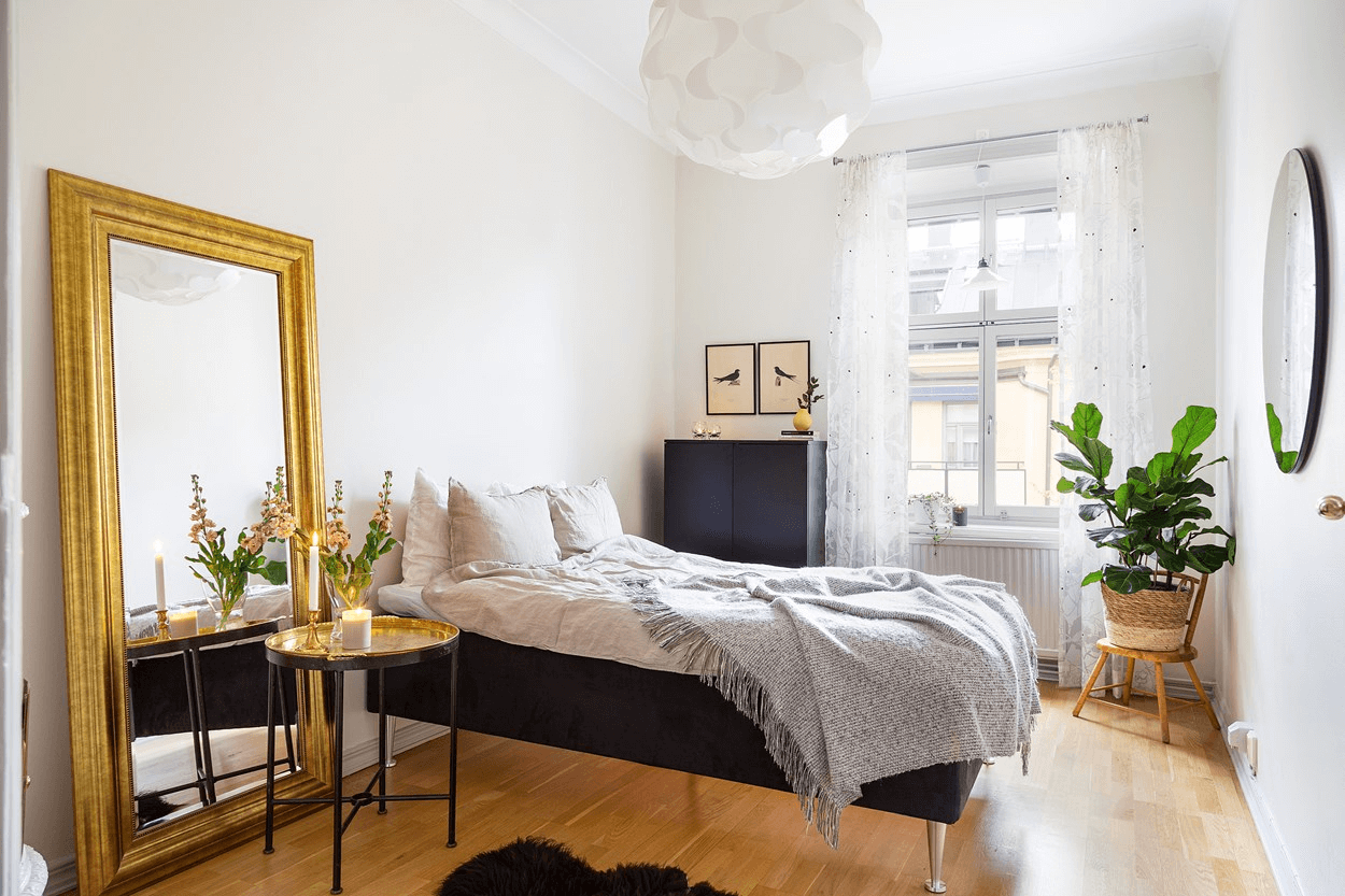 this is a minimal Scandinavian styled bedroom with a large golden brass mirror, and double bed